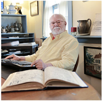 Harry Bellangy seated at his desk with an open book in front of him